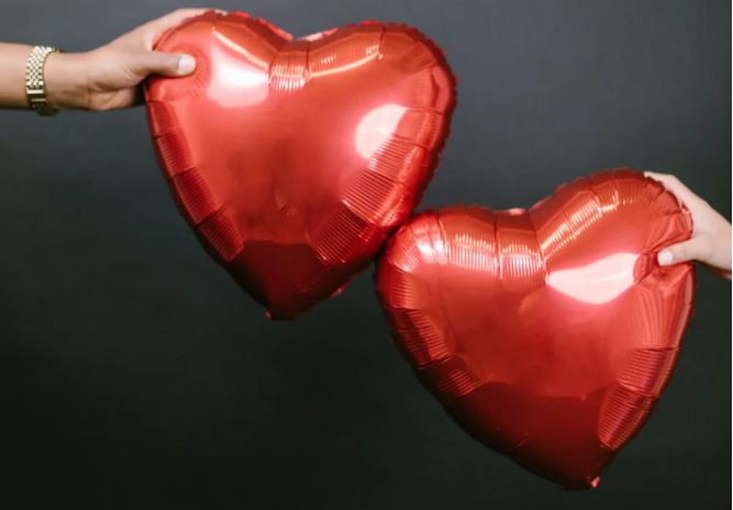 deux ballons en forme de coeur chacun tenu par un homme et une femme